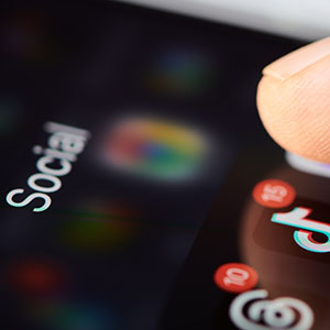 A finger tapping a phone screen with social media app icons, representing how social media can hurt a divorce case.