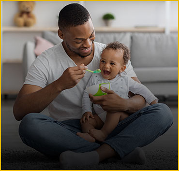 Father feeding baby: Illustrating paternity legal services.