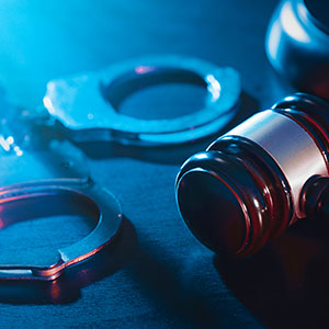 Handcuffs and a gavel under blue light, representing criminal defense and legal justice.