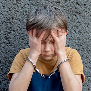 Handcuffed child covering face, symbolizing juvenile crimes and legal defense.