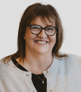 Office Administrator Beth Colbert smiling, wearing glasses and a white cardigan.